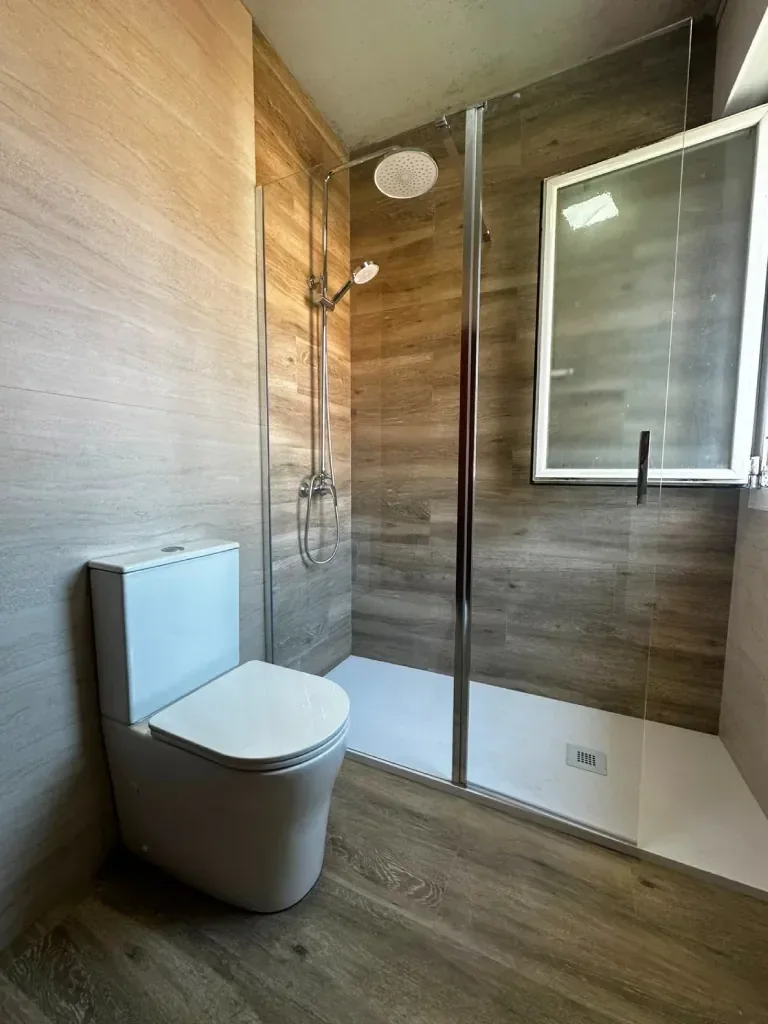 Zona de ducha con mampara de cristal y revestimiento efecto madera