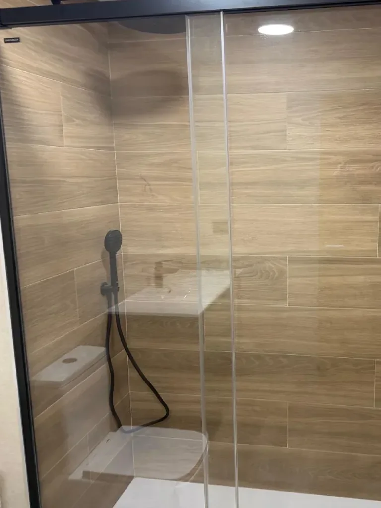 Revestimiento imitación madera clara en ducha con mampara